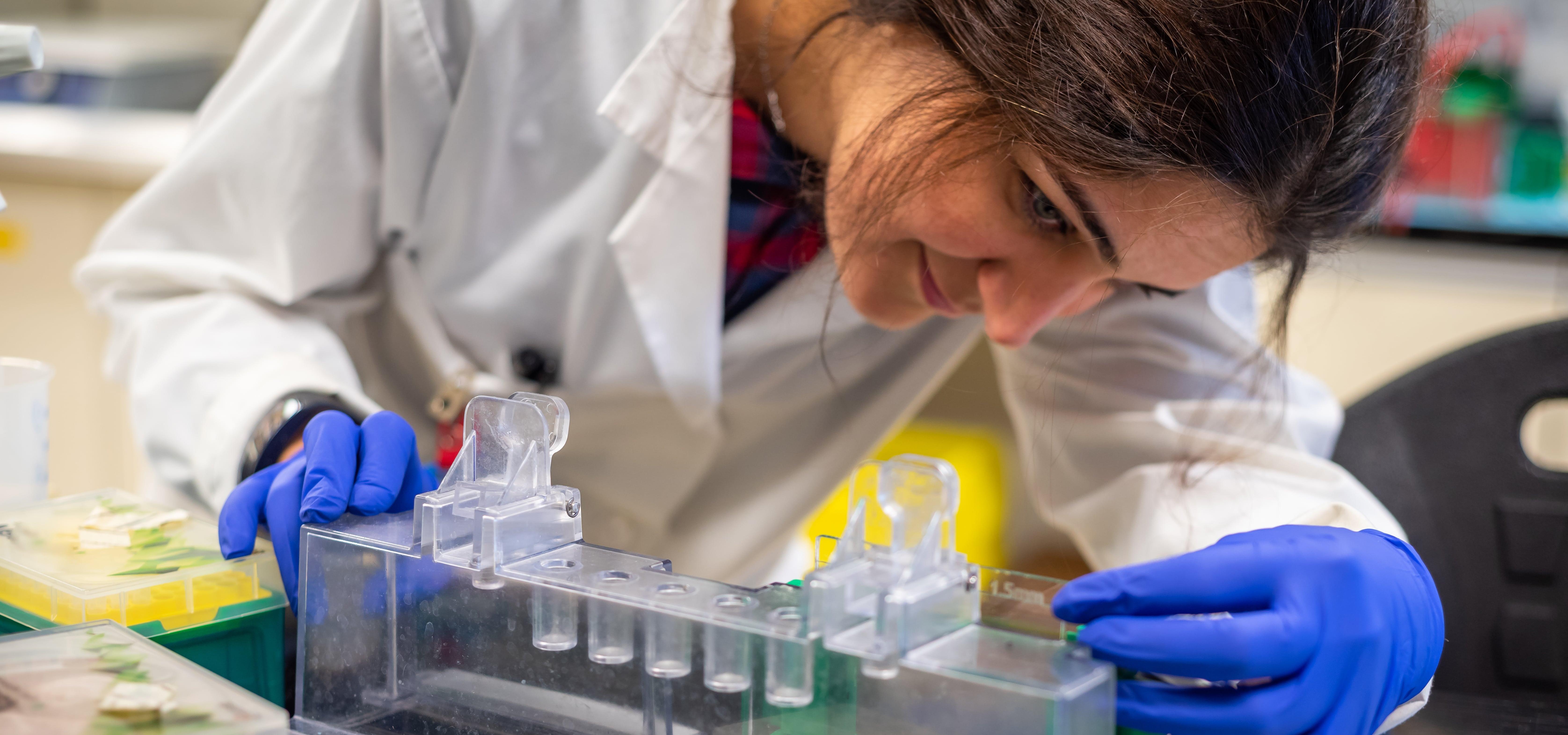Photo of a young woman in a lab coat studying test tubes